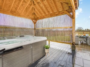 Uma banheira de hidromassagem sob um pérgola de madeira com um painel de bambu ao fundo.
