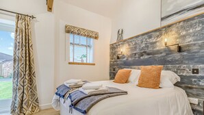 Un dormitorio con cama, cortinas, una ventana, una lámpara fijada a la pared y cabecera de madera.
