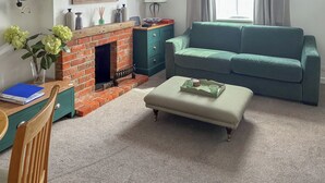 A cozy living room with a brick fireplace, teal sofa, and a striped ottoman. - 2 bedroom accommodation in Stockbridge (Stockbridge)
