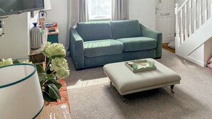 A living room with a green sofa, a striped ottoman, a TV, and a window with curtains. - 2 bedroom accommodation in Stockbridge (Stockbridge)
