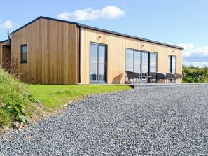 A modern building with wooden siding, large sliding glass doors, and a gravel driveway.