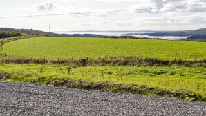 A rural landscape with a gravel road, green fields, and a distant body of water under a partly cloudy sky.