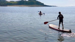 A calm lake with kayaks and a paddleboarder.