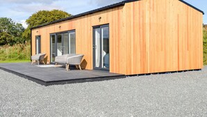 A modern wooden cabin with a deck, two glass sliding doors, and a wicker sofa.