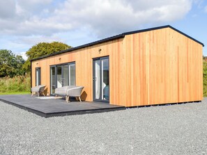 Une cabane moderne en bois, dotée d’une terrasse, de deux portes coulissantes en verre et d’un canapé en osier.
