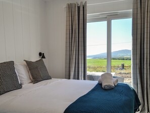 A bedroom with a bed, two pillows, a lamp, and a view of a landscape through a window.