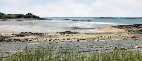 A beach with rocky terrain, a tent, and a person walking.