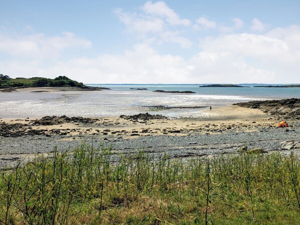 A beach with rocky terrain, a tent, and a person walking.
