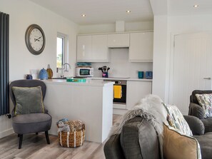 A modern kitchen with white cabinets, a microwave, and a sink. There is a wicker basket on the floor and a grey sofa with a fluffy throw.