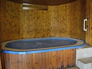 A wooden spa area with a hot tub, a wooden wall, and a tiled floor.