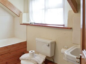 A bathroom with a wooden floor, a white toilet, a white bathtub, and a window with a wooden shelf above it.