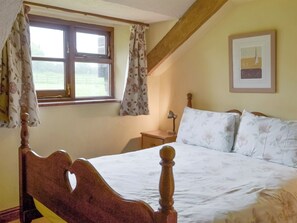 A bedroom with a wooden bed frame, a nightstand, a lamp, and a window with floral curtains.