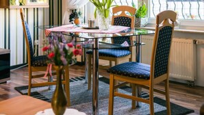 A dining area with a glass table, chairs with blue cushions, a vase with flowers, and a window with curtains.