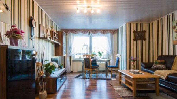 A cozy living room with striped wallpaper, a wooden coffee table, a sofa, and a dining area with chairs and a table.