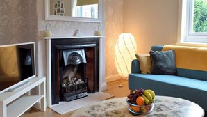Una sala de estar con chimenea, un sofá, un televisor y una mesa con frutero.