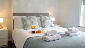 Una cama bien tendida con almohadas, una bandeja de fruta y croissants, y toallas en una habitación de hotel.