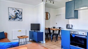 En moderne stue med sofa, fjernsyn, spiseområde med stole og et køkken med komfur.