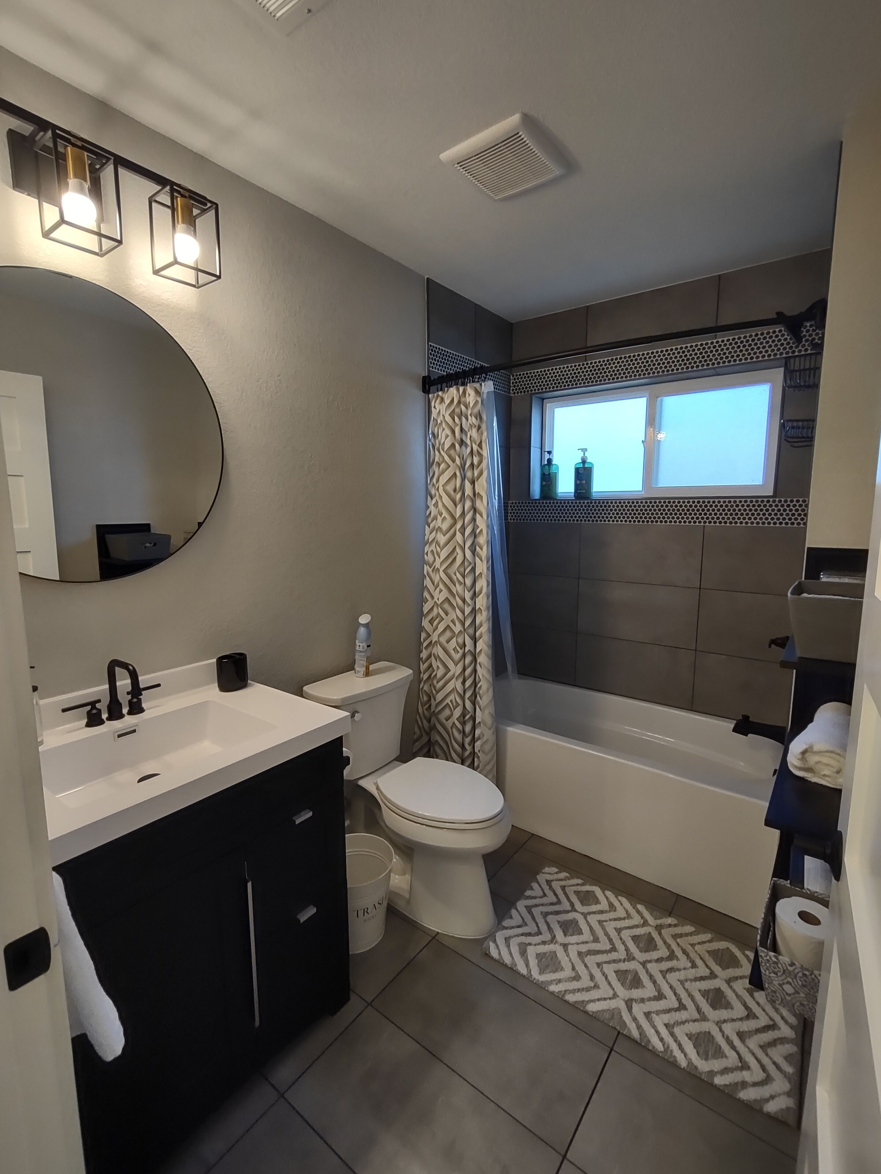 A modern bathroom with a white sink, black vanity, a toilet, and a bathtub.