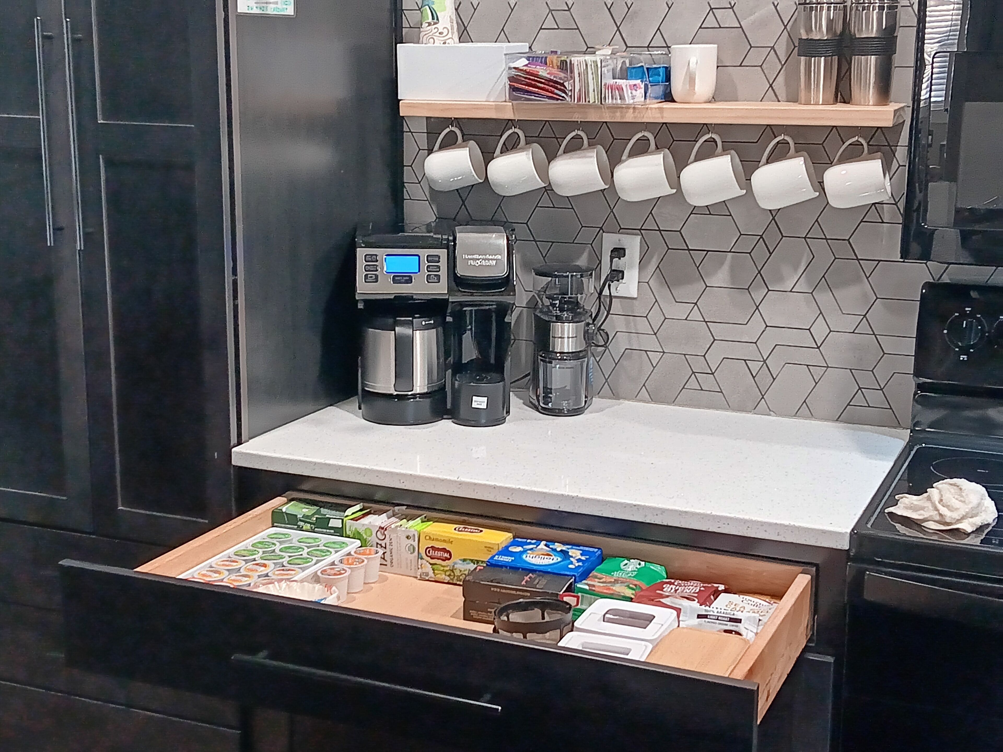 A kitchen with a coffee maker, a blender, and a drawer with food items.