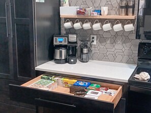 Una cocina con cafetera, licuadora y un cajón con alimentos.