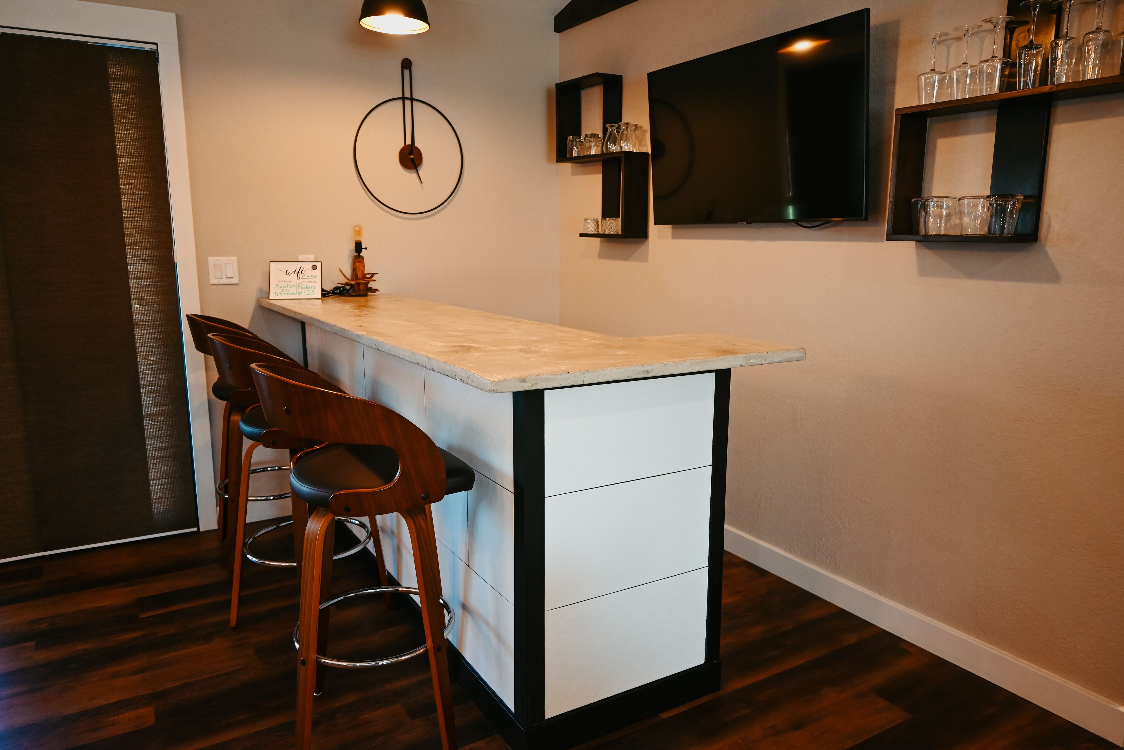 A kitchen with a bar area, wooden chairs, a white countertop, and a black shelf with glassware.