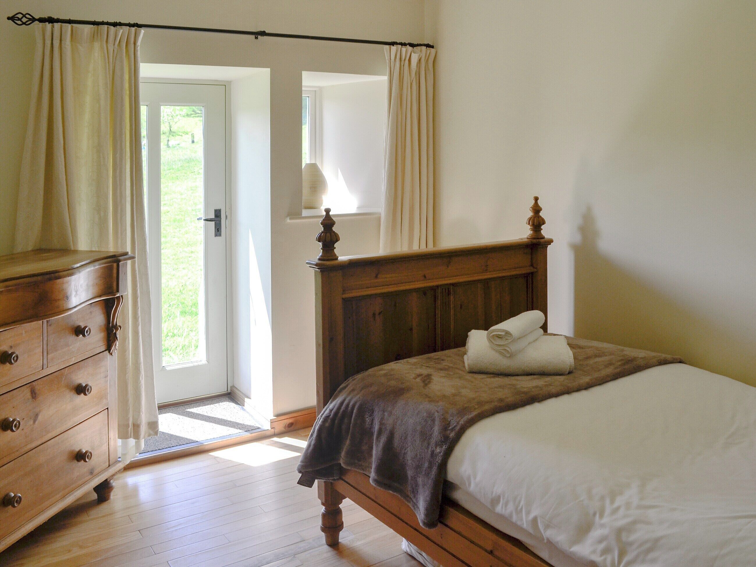Un dormitorio con una cama de madera, un aparador y una puerta que da a un espacio exterior luminoso.
