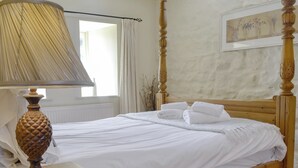 Un lit bien fait, avec du linge de lit blanc, une tête de lit en bois et une table de chevet avec une lampe.