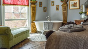 A traditional bathroom with a freestanding bathtub, a green armchair, and a window with a red curtain. - 1 bedroom accommodation in Hastings (Hastings)