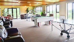 Une salle de billard équipée d’une table de billard, de fauteuils en cuir et de grandes fenêtres.