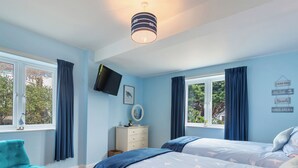 A bedroom with two beds, a TV, a dresser, and a window with curtains. - Min y Traeth (By the Beach) (Morfa Nefyn, near LLyn Peninsula)