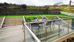 A glass deck with outdoor seating, a barbecue grill, and a stone wall in the background. - Min y Traeth (By the Beach) (Morfa Nefyn, near LLyn Peninsula)