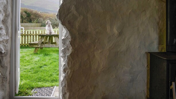 A rustic stone wall with a window revealing a wooden deck and a grassy yard. - 2 bedroom accommodation in Clynnog Fawr (Clynnog Fawr)