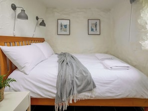 Uma cama de solteiro com roupa de cama branca, um cobertor cinza e duas obras de arte emolduradas na parede.
