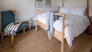 A neatly arranged bedroom with a single bed, a desk, and a chair. There are two framed pictures on the wall, a shelf above the bed, and a lamp on the nightstand. - 2 bedroom accommodation in Clynnog Fawr (Clynnog Fawr)