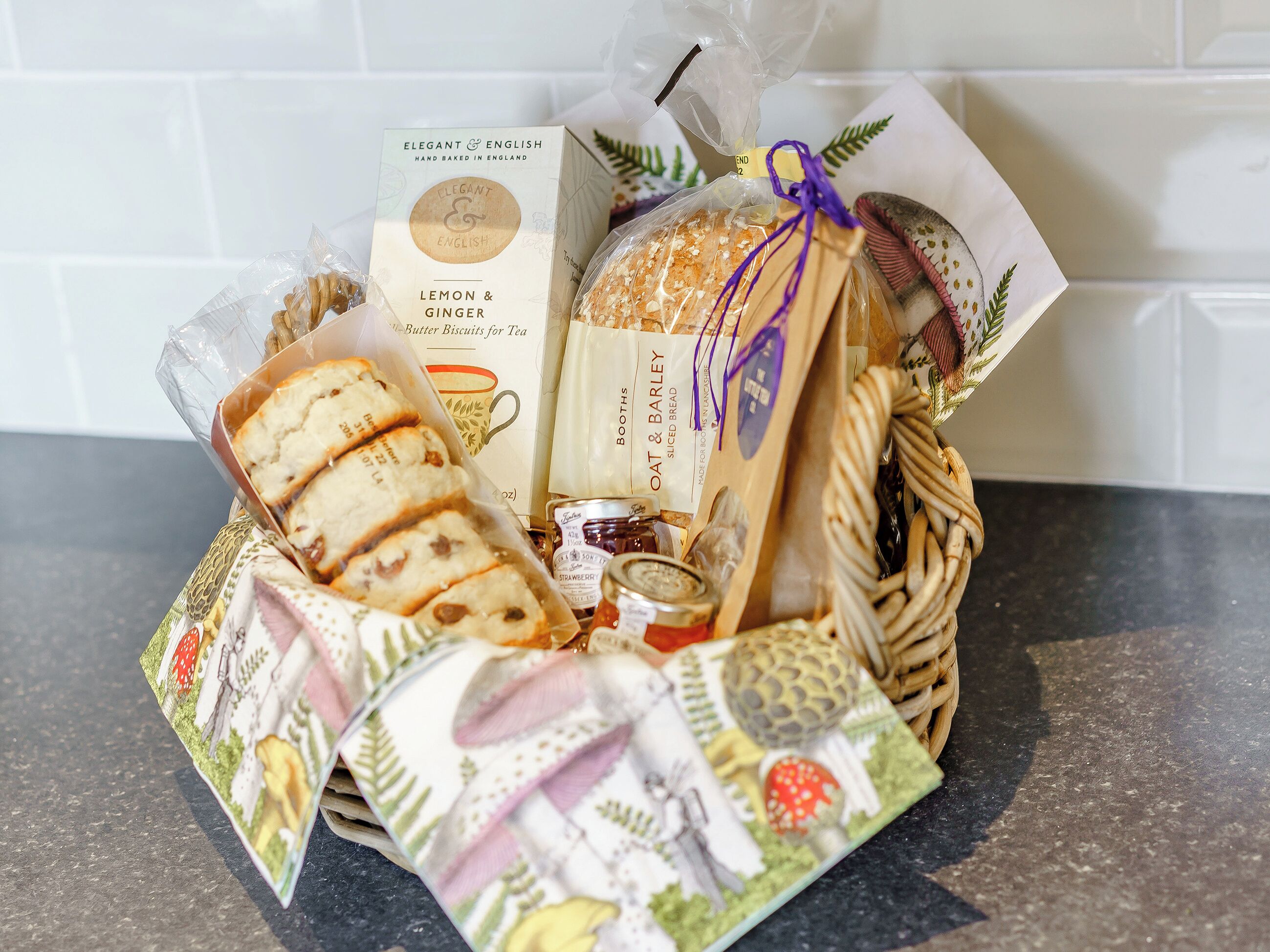 Un panier-cadeau contenant divers produits de boulangerie et une boîte étiquetée « Biscuits au beurre élégants, saveur citron et gingembre, parfaits pour accompagner le thé ».
