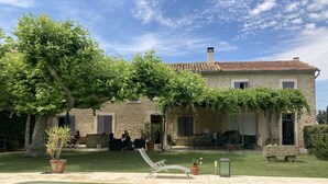 Una casa de pedra amb piscina, mobiliari exterior i una pèrgola coberta de vidatge.