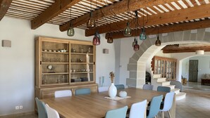 Zona de menjador amb taula i cadires de fusta, un armari de vidre amb plats, i una escala que condueix a una altra habitació.