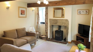 A living room with a sofa, a television, a fireplace, and a stone mantle. - Godfrey Hole Cottage (Godfrey Hole near Carsington Water)