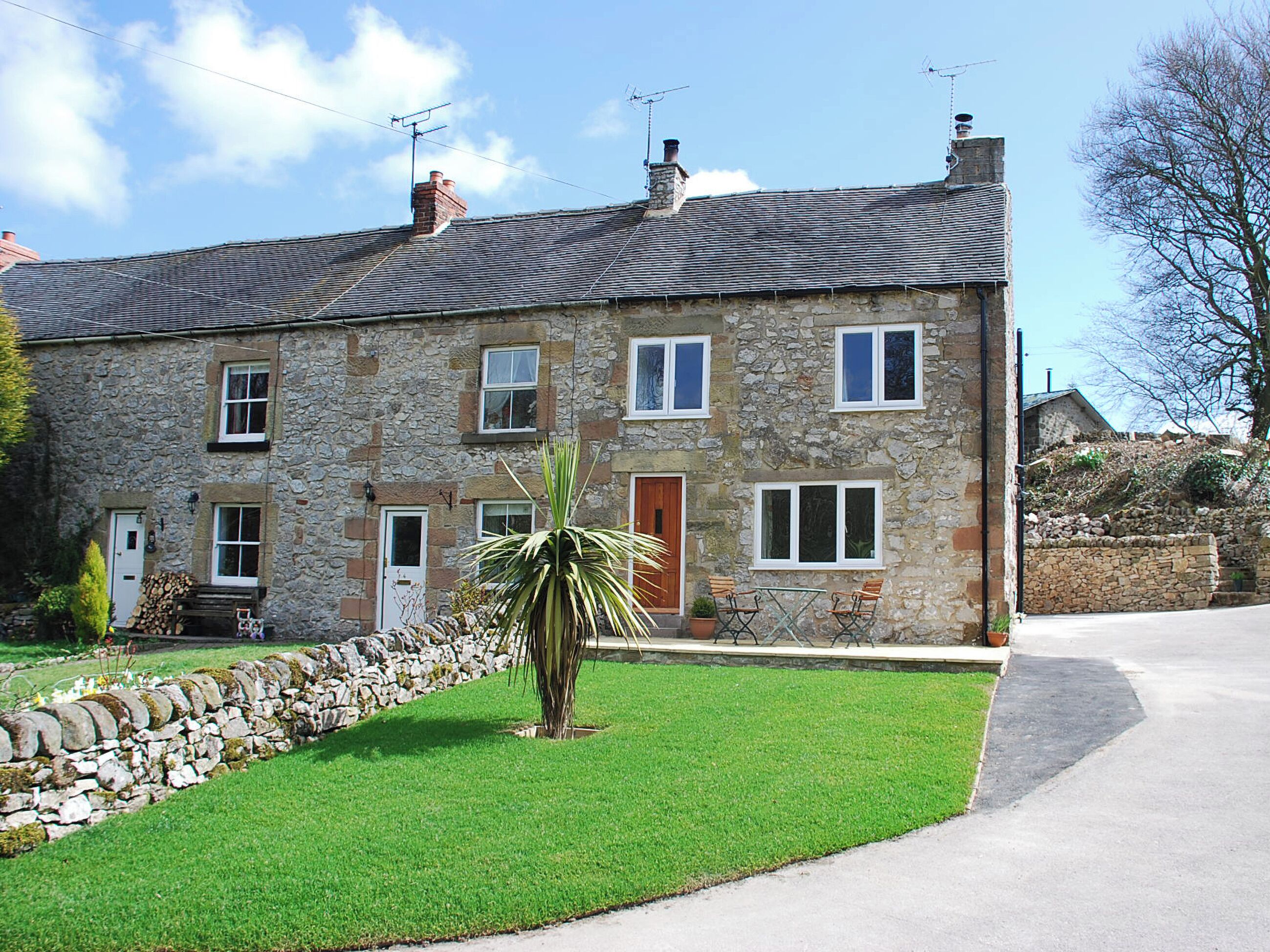A stone house with a tiled roof, multiple windows, and a small lawn with a palm tree.