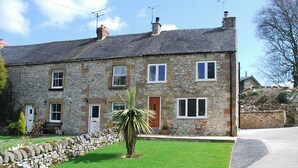 A stone house with a tiled roof, multiple windows, and a small lawn with a palm tree. - Godfrey Hole Cottage (Godfrey Hole near Carsington Water)