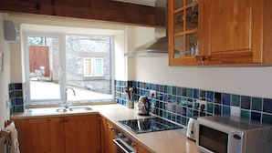 A kitchen with wooden cabinets, a sink, a stove, a dishwasher, and a microwave. - Godfrey Hole Cottage (Godfrey Hole near Carsington Water)