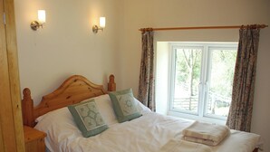 A bed with a wooden headboard, two decorative pillows, a white blanket, and a window with curtains. - Godfrey Hole Cottage (Godfrey Hole near Carsington Water)