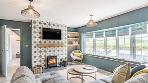 A modern living room with a fireplace, comfortable seating, a TV, and large windows offering a view of the outdoors. - 3 bedroom accommodation in Llanerfyl, near Welshpool (Llanerfyl, near Welshpool)