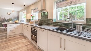 A modern kitchen with white cabinetry, a large island, a built-in oven, and a window with a view of greenery. - 3 bedroom accommodation in Llanerfyl, near Welshpool (Llanerfyl, near Welshpool)
