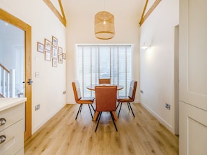 A dining area with a round table, two chairs, a hanging light fixture, and a window with blinds.