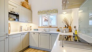 Eine moderne Küche mit weißen Schränken, einem eingebauten Backofen, einem Fenster mit Vorhängen und Holzboden.