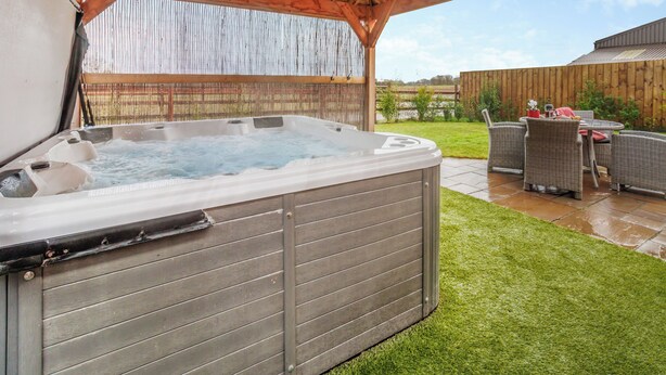 Ein Whirlpool unter einer Holzpergola mit einer Terrasse und Korbmöbeln.