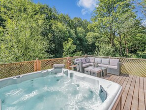 A hot tub surrounded by a wooden deck, with a seating area and a wooden fence.