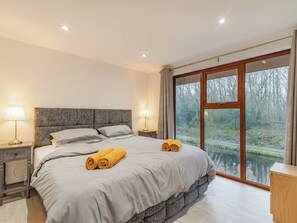 A bedroom with a large bed, two bedside lamps, a nightstand, and a view of a forest through a large window.