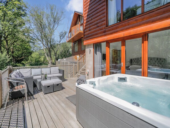 A wooden deck with outdoor furniture, a hot tub, and a view of a building with large windows.